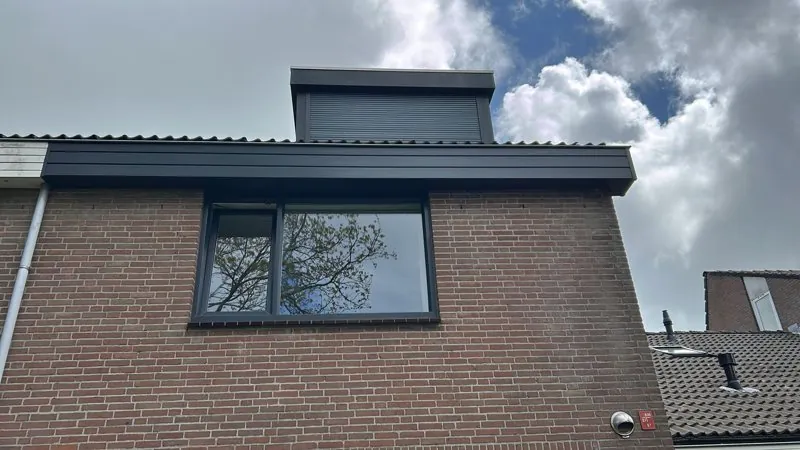 Antraciet dakkapel met breed raam op een bakstenen woning