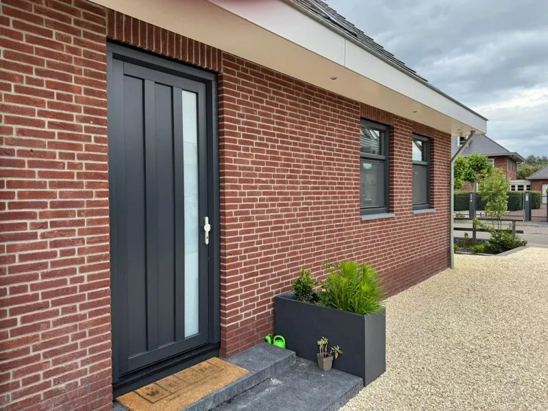 Antraciet kunststof voordeur met smal zijlicht in een rode bakstenen gevel